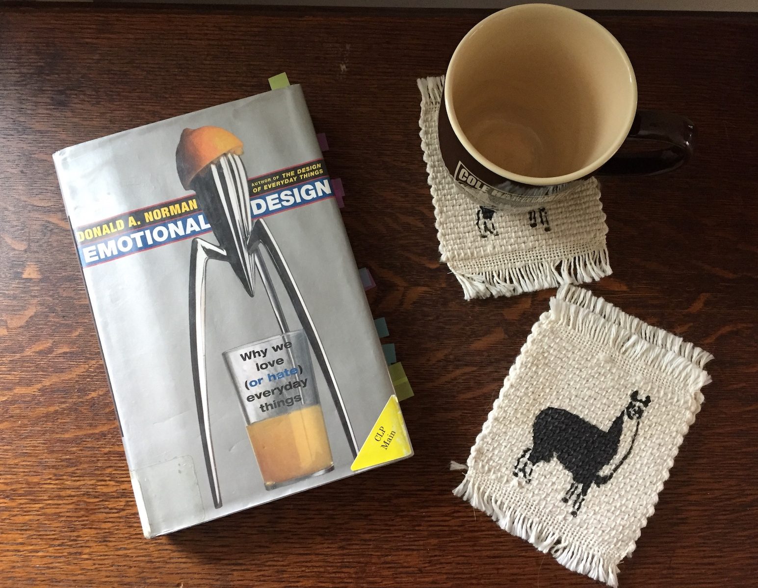 The book "Emotional Design" by Don Norman, sitting next to coasters depicting a llama and a brown coffee mug.