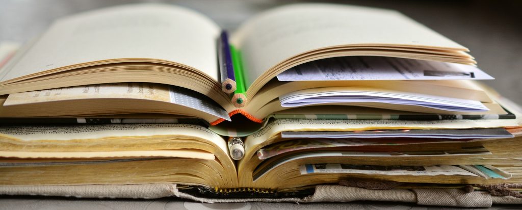 three dog-eared books stacked on top of one another, with pencils, paper, and sticky notes marking pages.